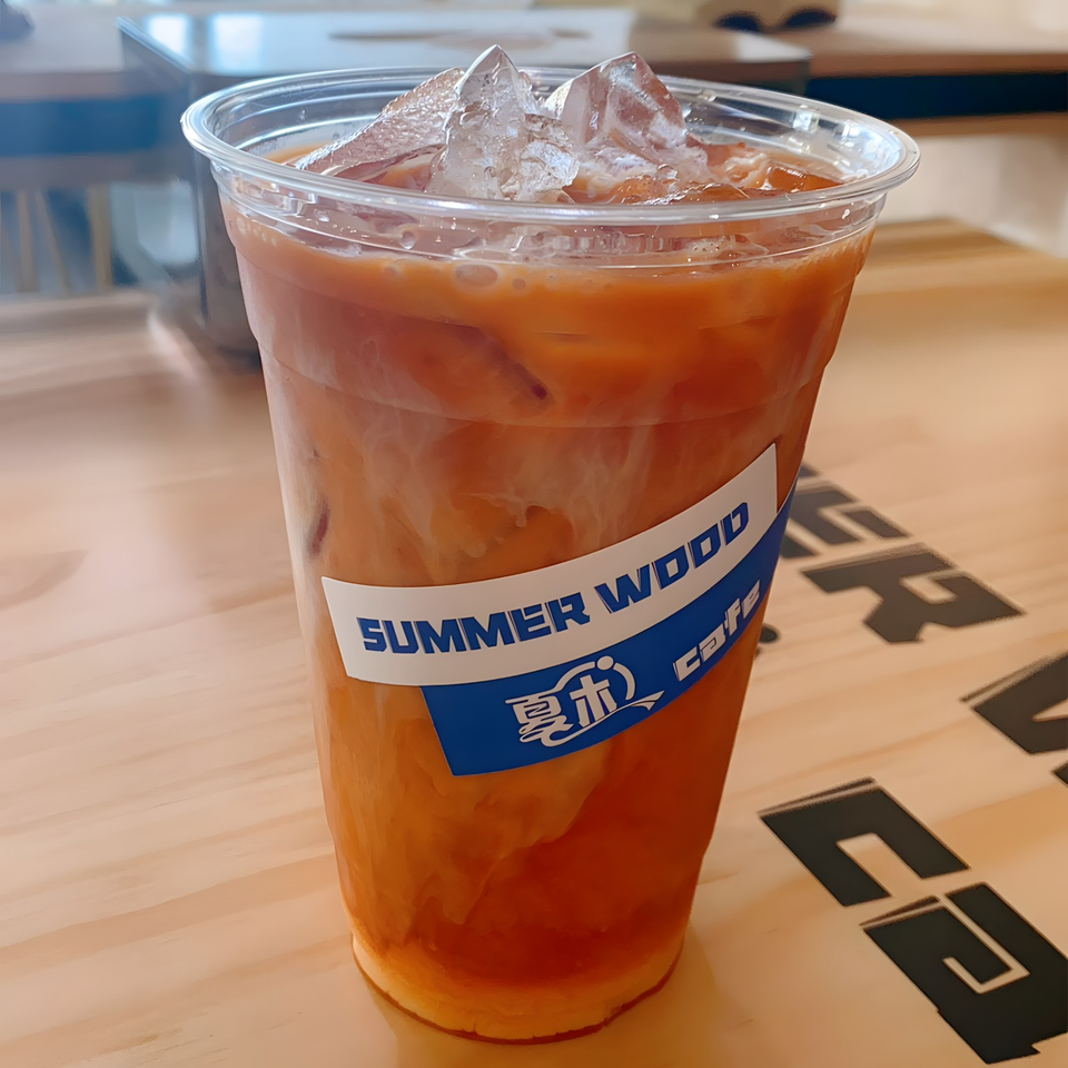 Iced Thai tea with a Summer Wood Cafe label on a light wooden table.