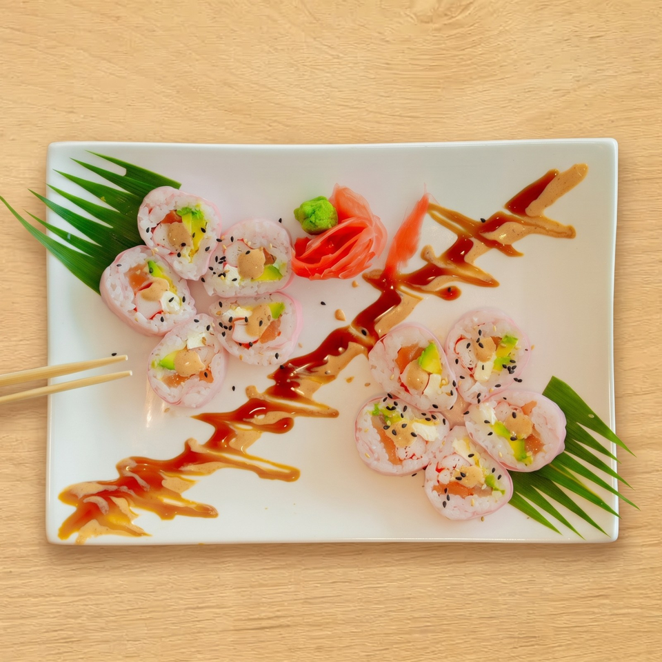 Pink sushi rolls with avocado, salmon, and cream cheese, drizzled with sauce on a white plate.