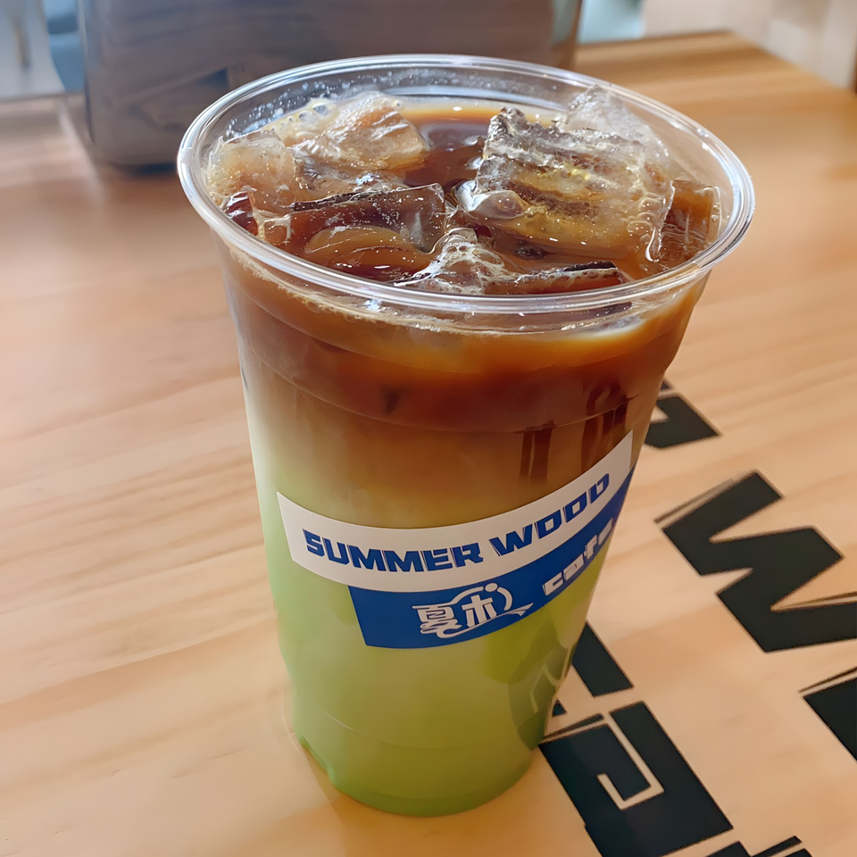 Iced matcha latte with coffee layers in a clear plastic cup on a wooden table.