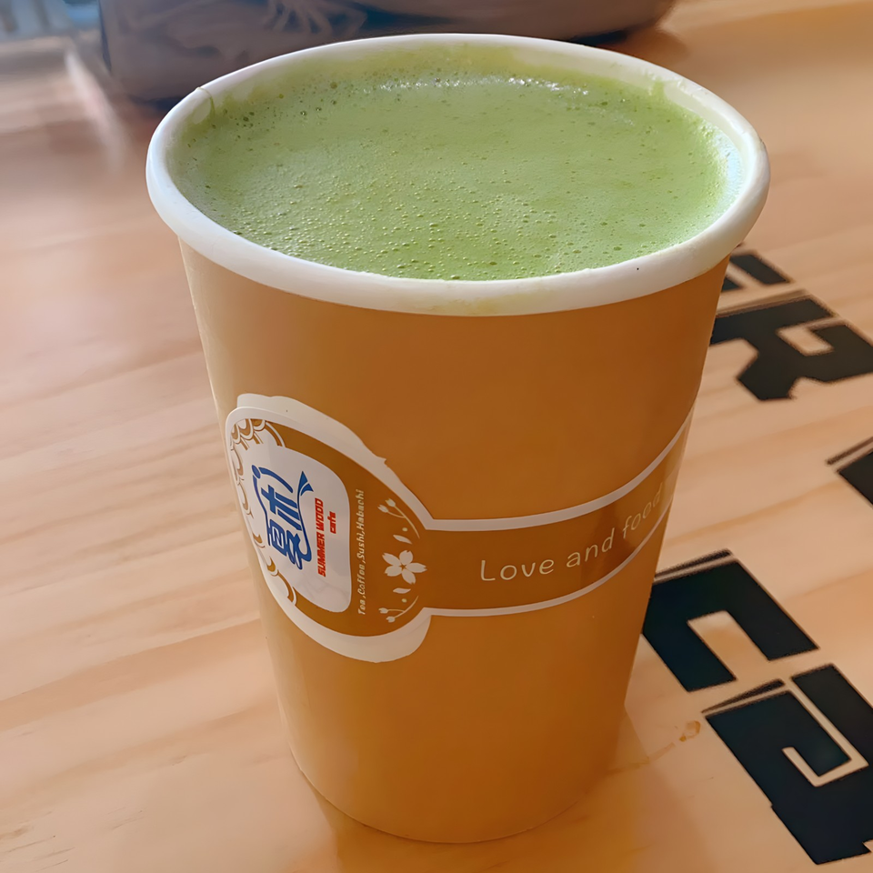 A Summer Wood Cafe matcha latte in a branded paper cup on a light wooden table.